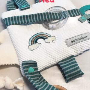 Sensorik Spielzeug für Babys. Geschenk zur Geburt und passend für Maxi Cosi. Abgebildet ist ein Quadratisches, flaches Kissen mit Überzug auf beigem Cordstoff und einem aufgestickten Regenbogen. Die Farben im Regenbogen in mint, petrol und dunkelgrün passen genau zu den angenähten Schleifen, mit denen die Rassel und die beiden Beißringe am Kissen befestigt sind.